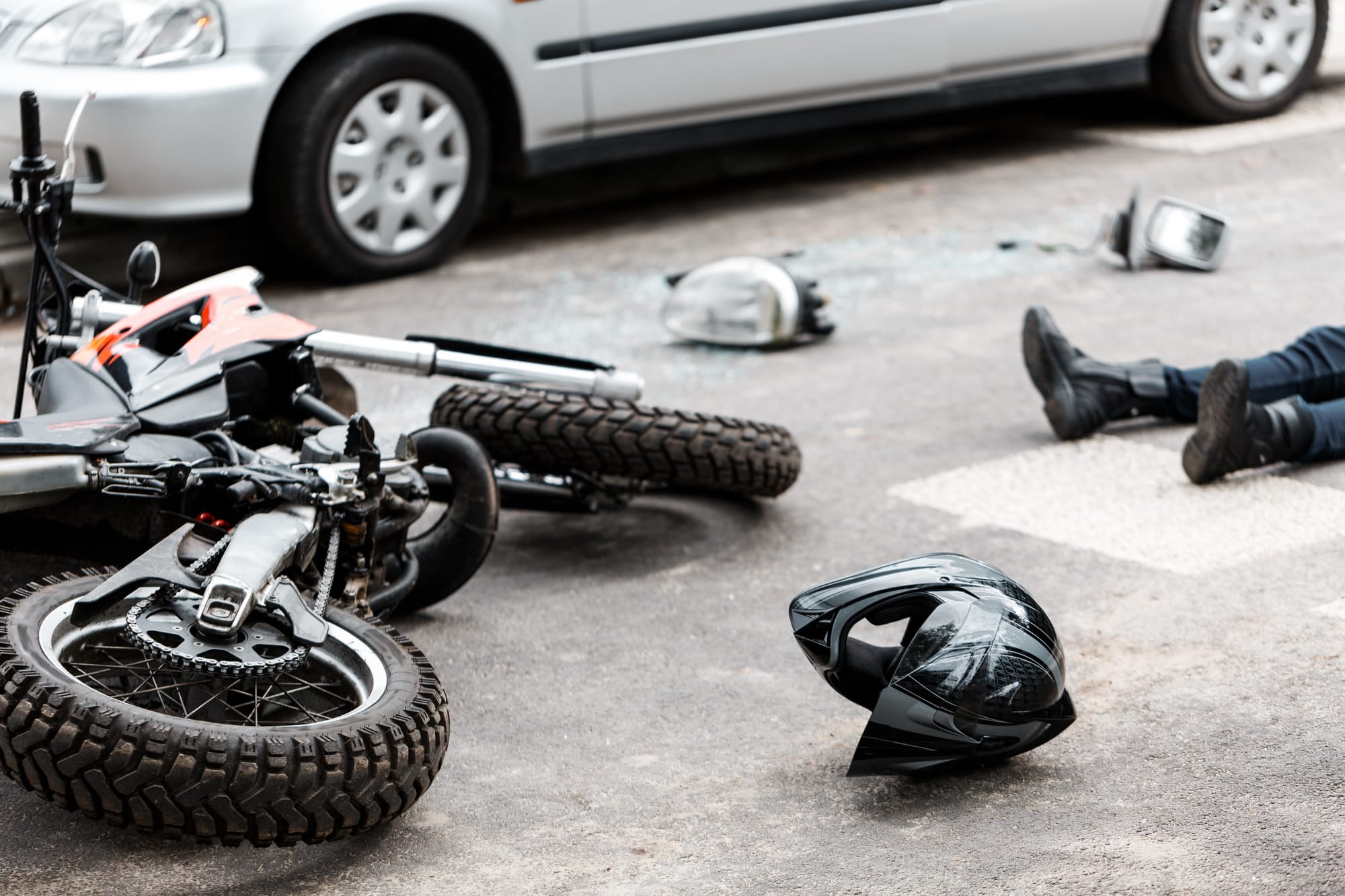 Legs of person lying on the road in the photo of motorcycle and car accident