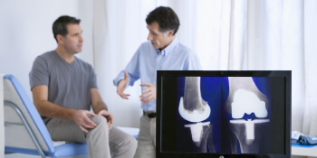 Doctor explaining knee X-ray results to male patient during consultation for car accident or workers’ compensation knee injury treatment