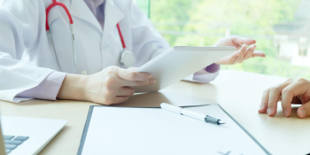 Doctor in white coat with stethoscope using tablet to discuss treatment with patient during medical consultation for car accident or workers’ compensation injury
