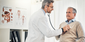 Doctor using stethoscope to examine senior male patient in medical office, checking for injuries from car accident or workers’ compensation claim