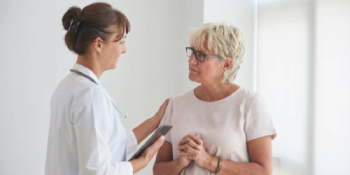 Female doctor in white coat holding clipboard while speaking compassionately with senior female patient during medical consultation for accident or workers’ compensation injury