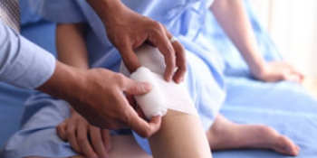 Doctor carefully applying white bandage to patient's knee during medical treatment for car accident or workers’ compensation injury