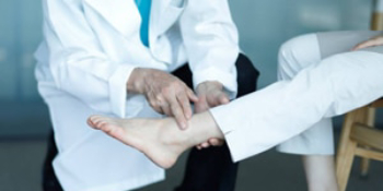 Doctor in white coat carefully examining and palpating a patient's ankle and foot during medical assessment for car accident or workers’ compensation injury